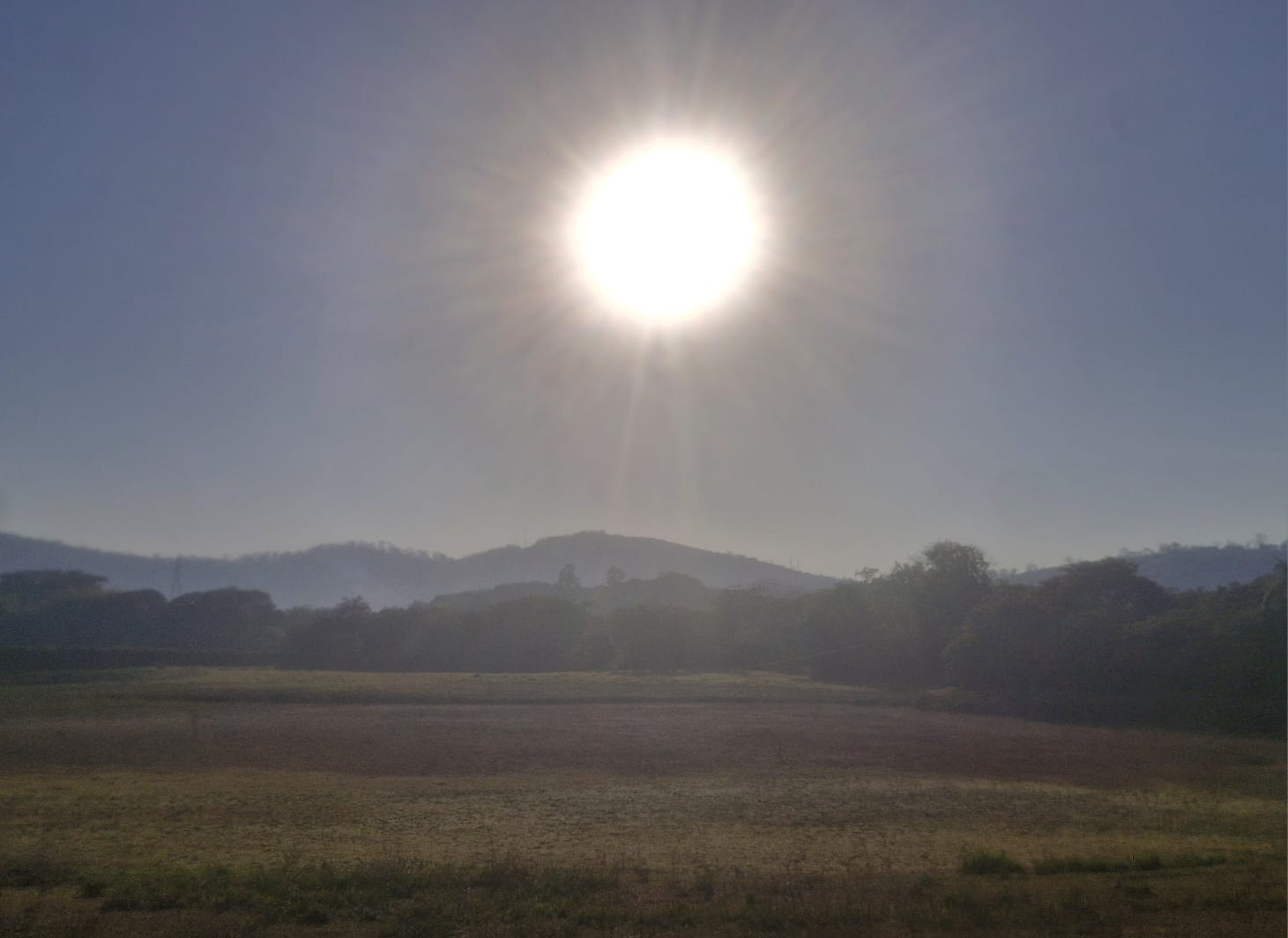 Nascer do sol com raios sobre colinas e campo aberto